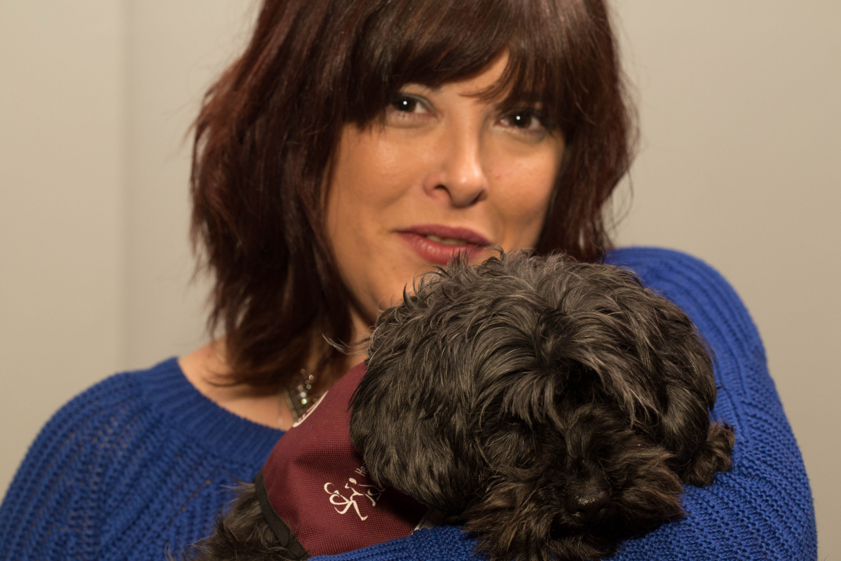Claire Holland holding a small dog with a maroon hearing dog coat on