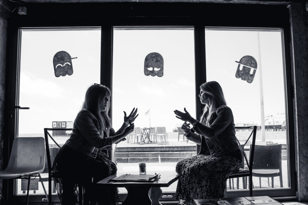 black and white photo of 2 ladies sat in a gaming cafe in front of a window signing