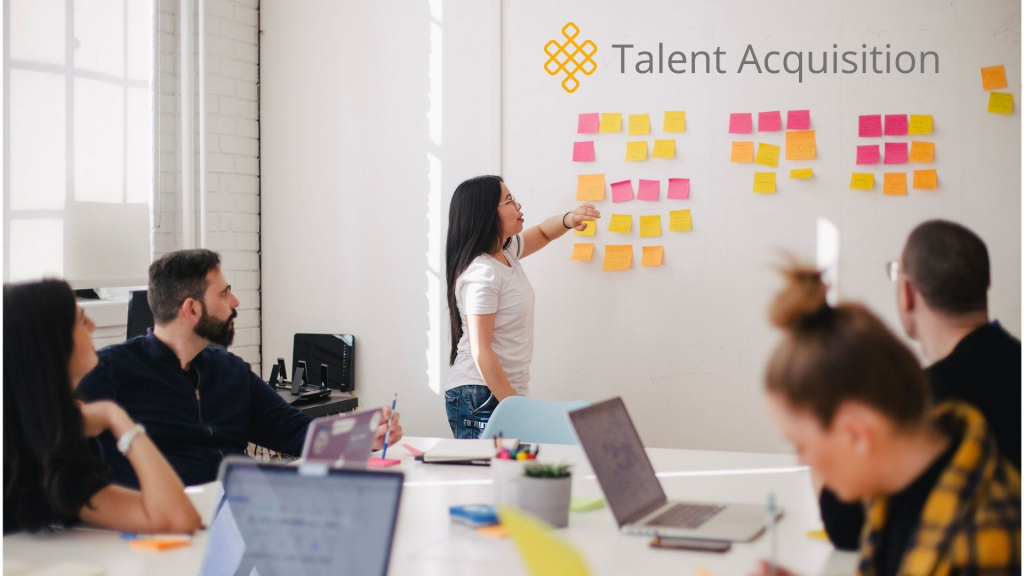 A team meeting with a woman standing in front of a white board entitled Talent Acquisition