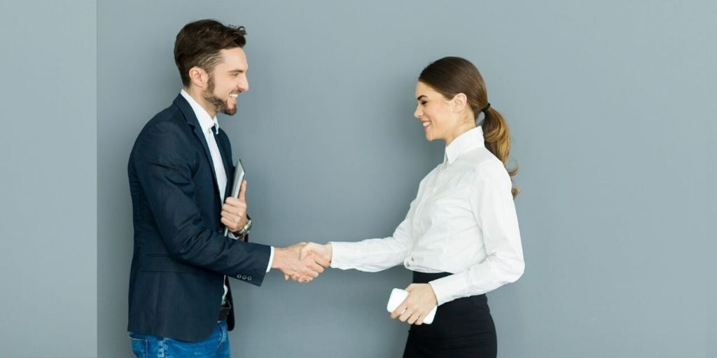 Learn how to communicate with Deaf and Hearing Impaired Colleagues. A man and woman in business clothes shake hands and smile at each other
