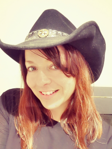 Jodie Bowles has medium length brown hair and is smiling at the camera wearing a cowboy hat and black tshirt