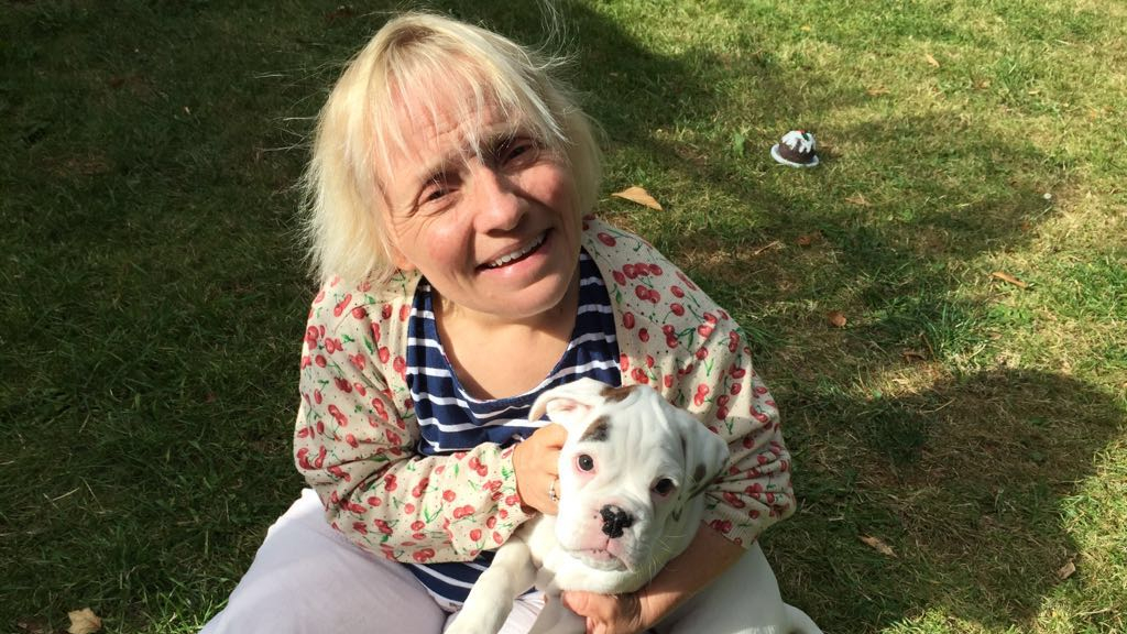 Becky Batten sitting on grass, holding a small white dog.