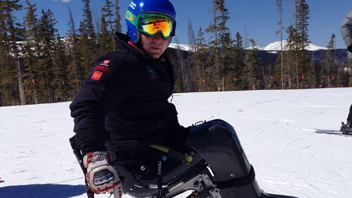 Andy Trollope on his skis, tree lined snow in the background and bright blue sky