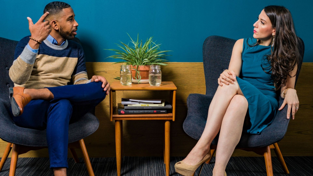 communication impairment - a smartly dressed man and woman sit opposite each other on comfortable chairs having a conversation. Both wear smart work clothes and make eye contact with each other