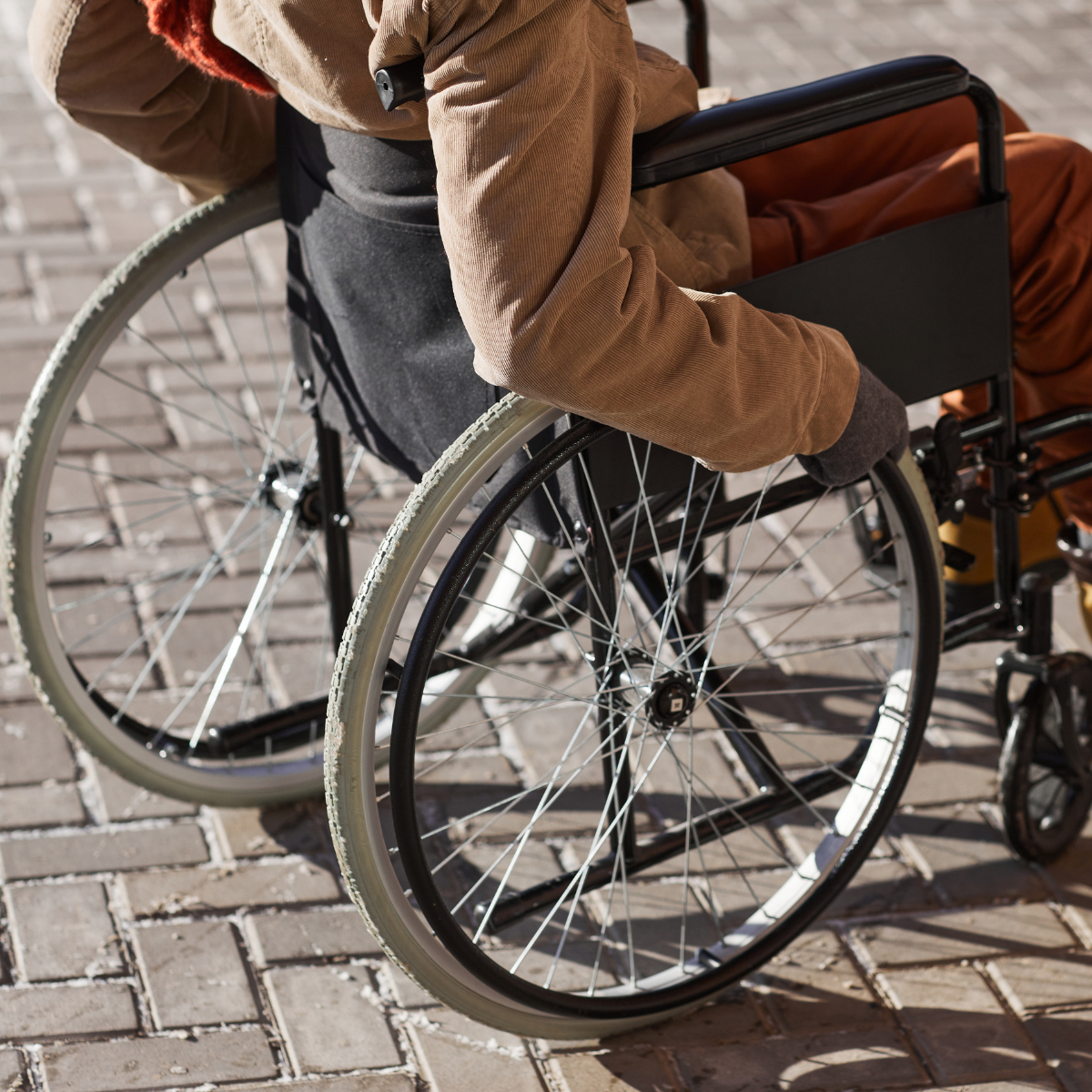 Wheelchair user facing away from camera, on the pavement. Head and shoulder are cropped out of photo