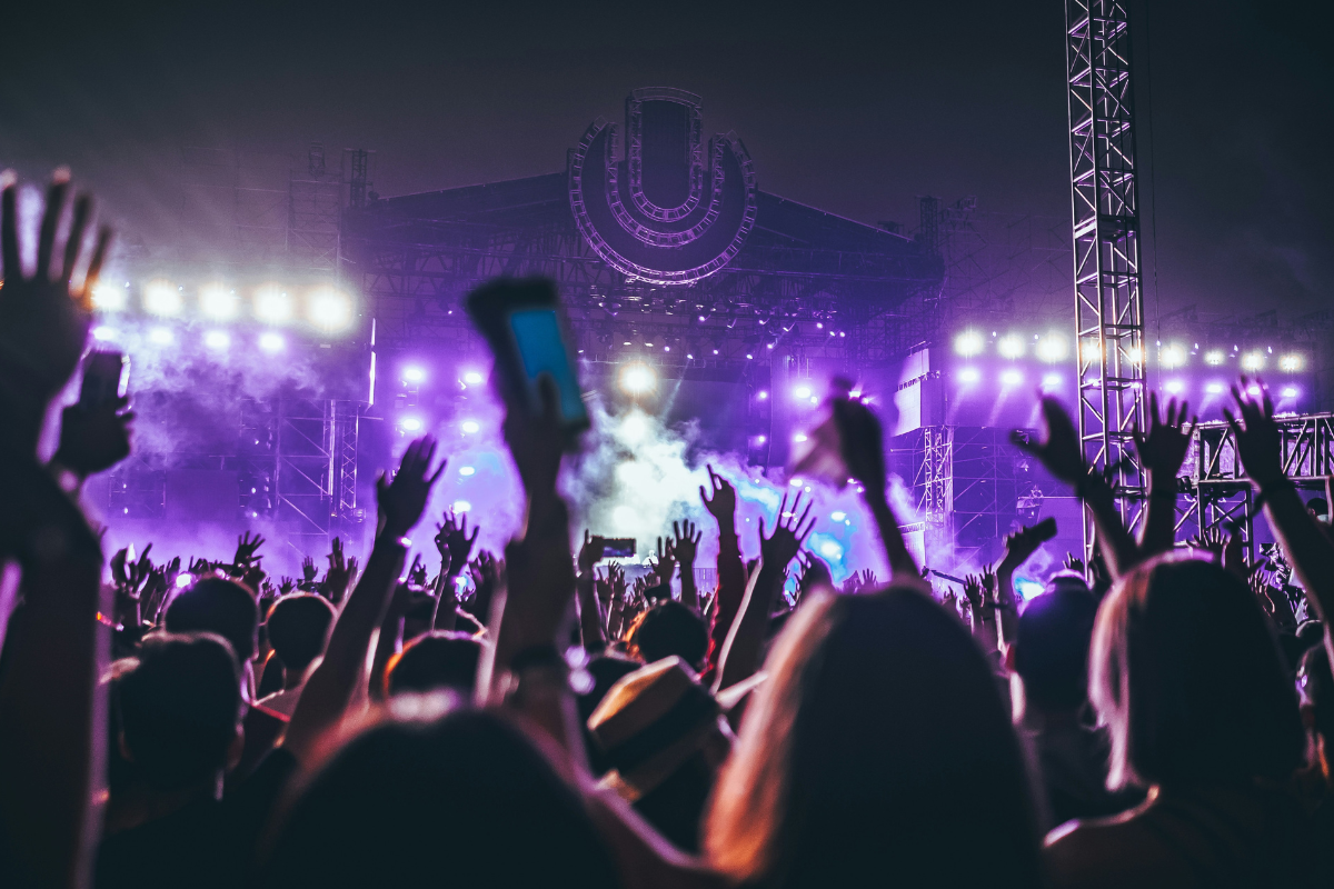 Festivals: a festival scene with people raising the hands in the air before a massive stage. There are purple lights