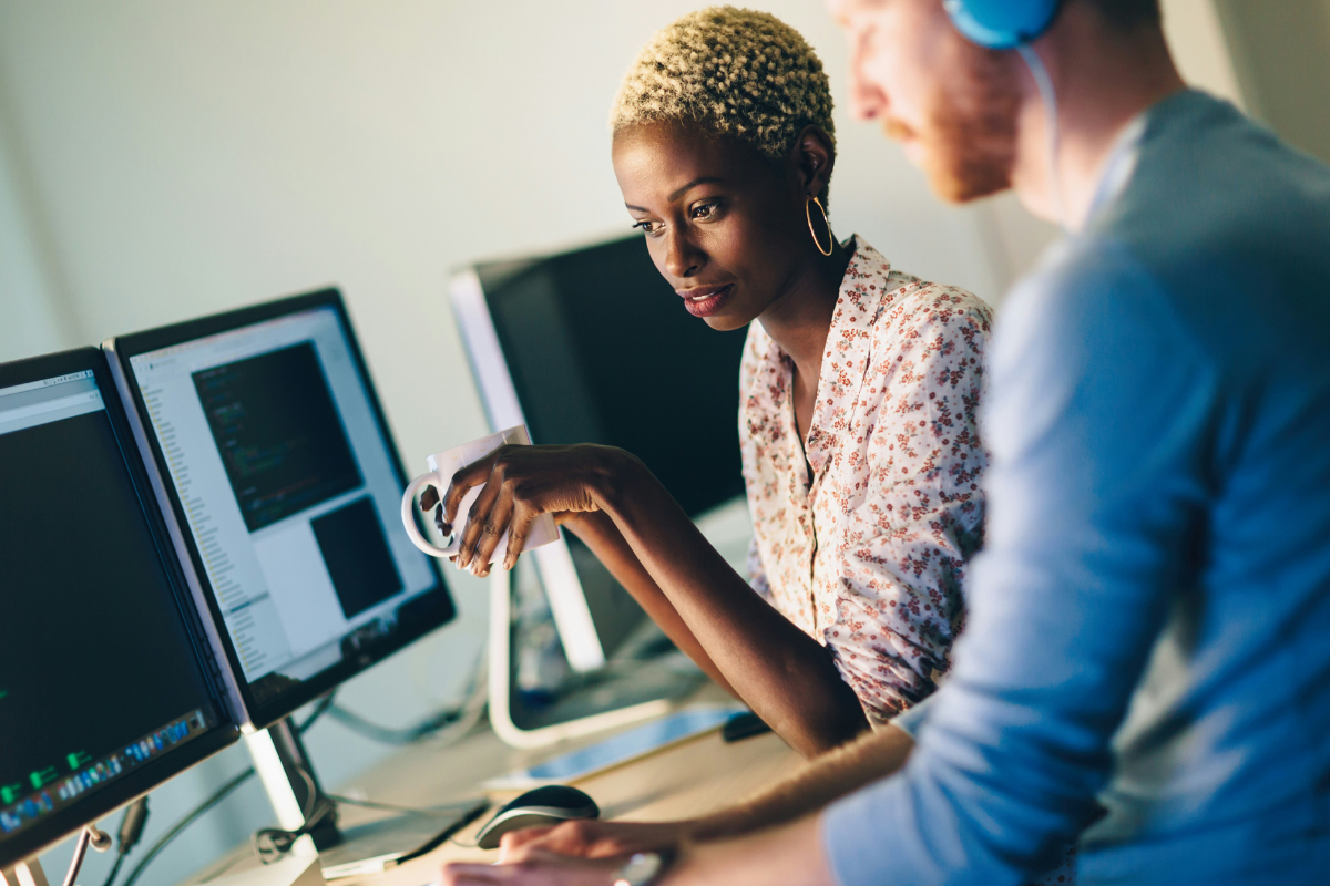 Cancer awareness: Two people are chatting around a big computer screen and sharing a cup of coffee